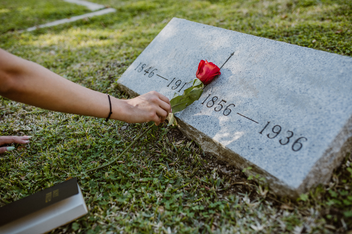 Person Hand Putting Red Rose on Gravestone