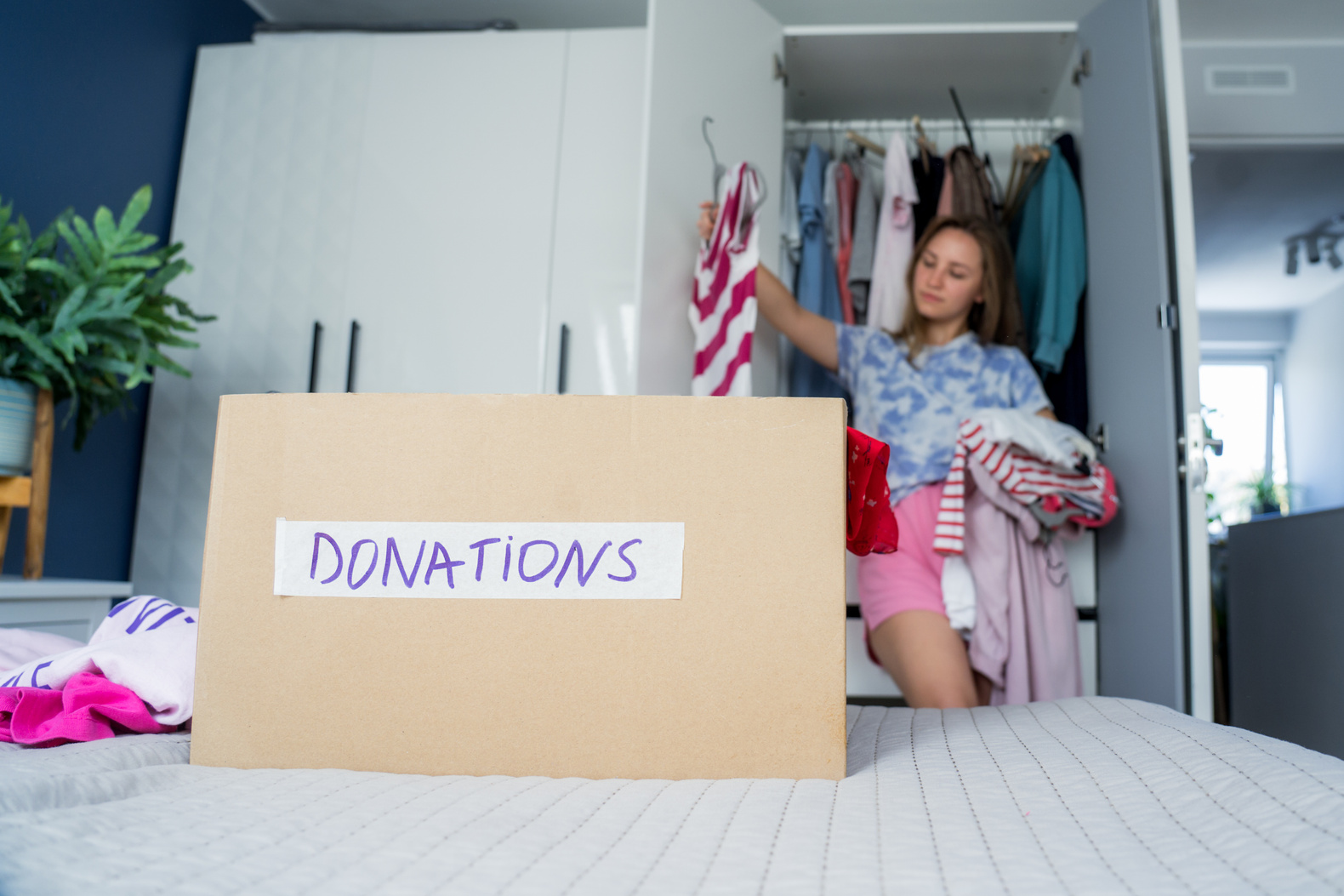 A Cardboard Box of Selected Clothes for Donating to a Charity Shop Standing on the Bed. Decluttering, Sorting Clothes, and Cleaning up. Reuse, Second-Hand. Conscious Consumer, Sustainability.